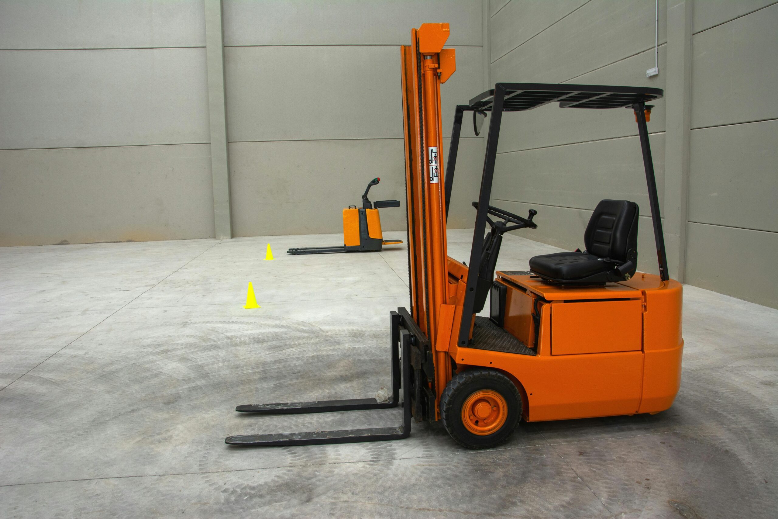 An orange forklift in a spacious warehouse with concrete floors and minimal equipment.